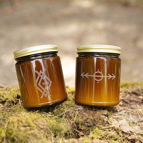 Woodsman limited edition laser etched nordic design soy candles in amber jars with gold lids on mossy log